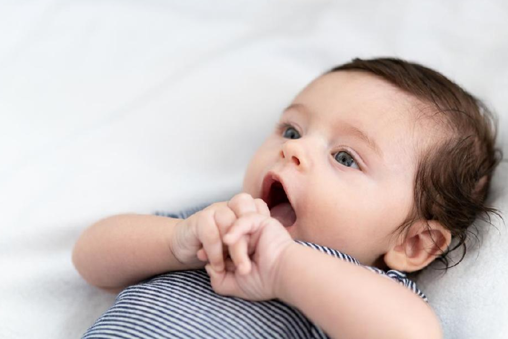 Bebê fofinho deitado segurando as mãos e com a boca aberta